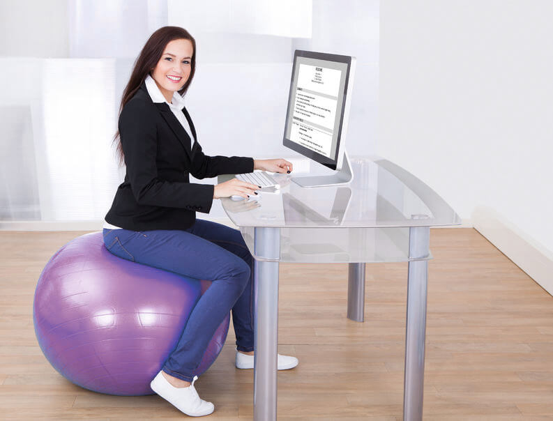 Frau sitzt auf einem Gymnastikball im Büro